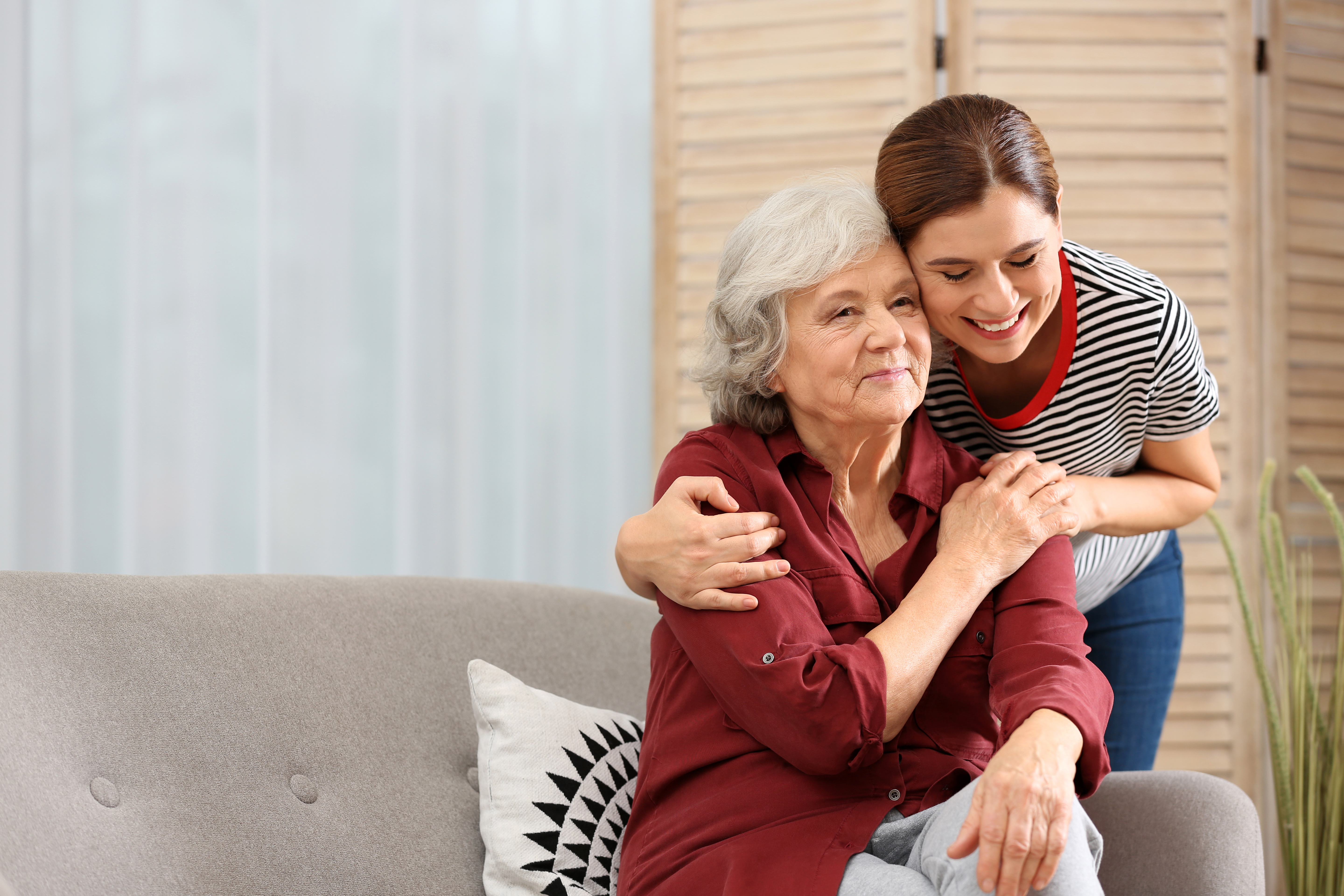 Elderly woman with female caregiver in living room. Space for te